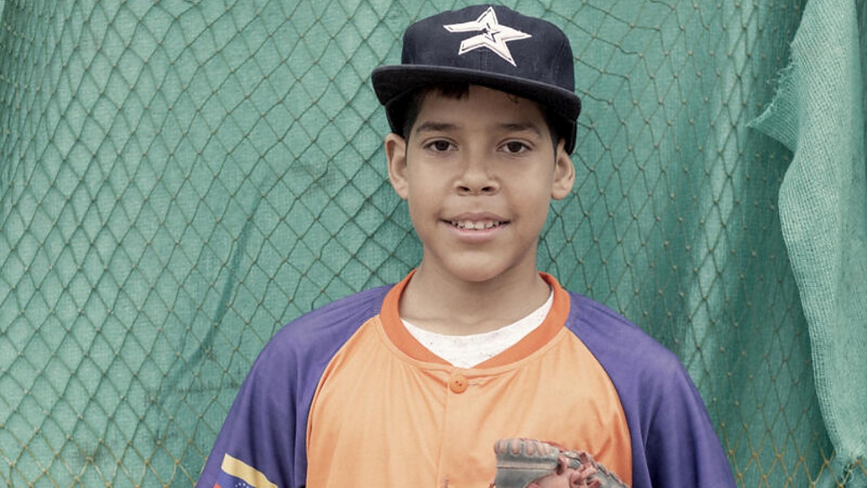 A young baseball player poses in his cap and uniform