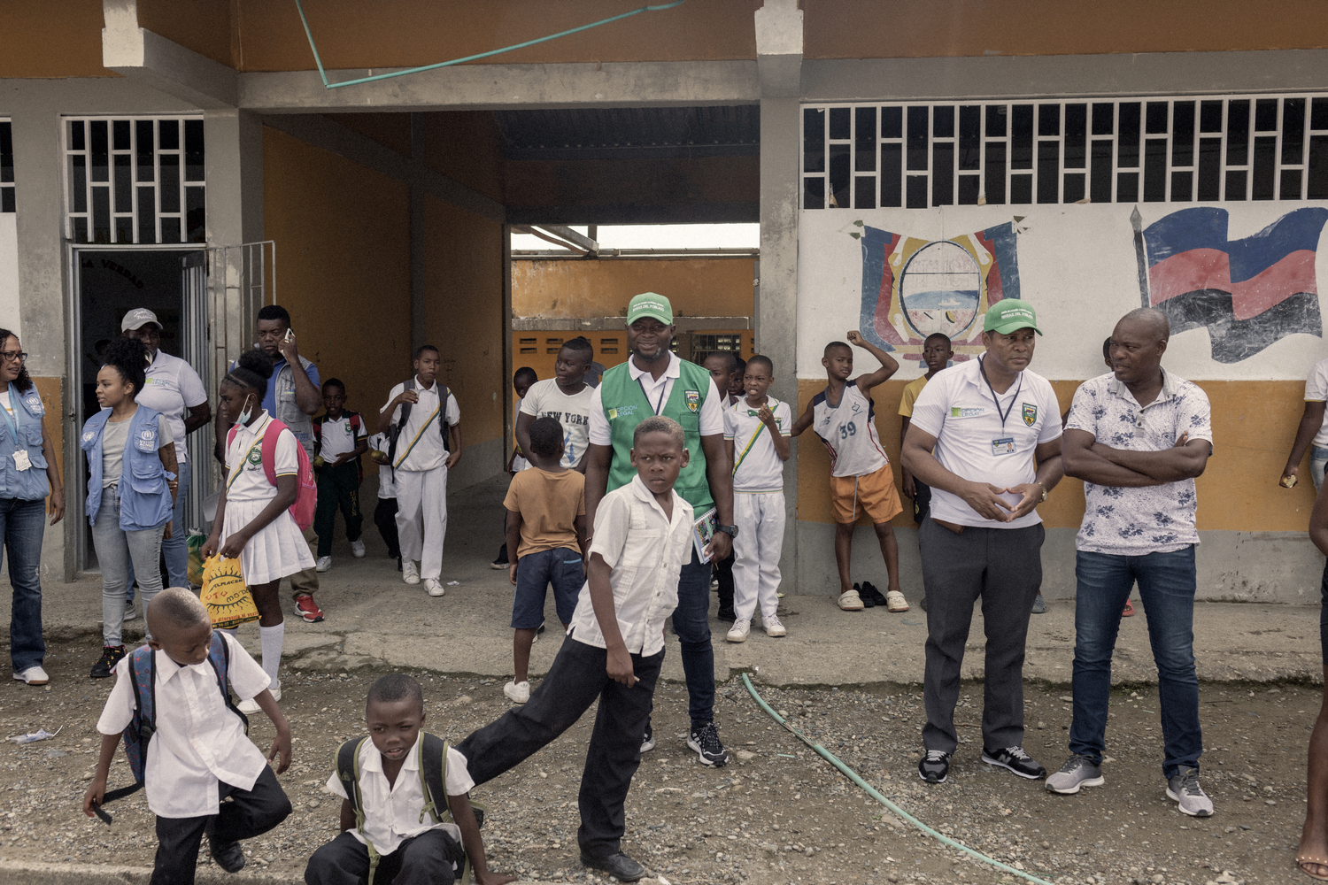 A man in a green vest and hat stands amongst school children,