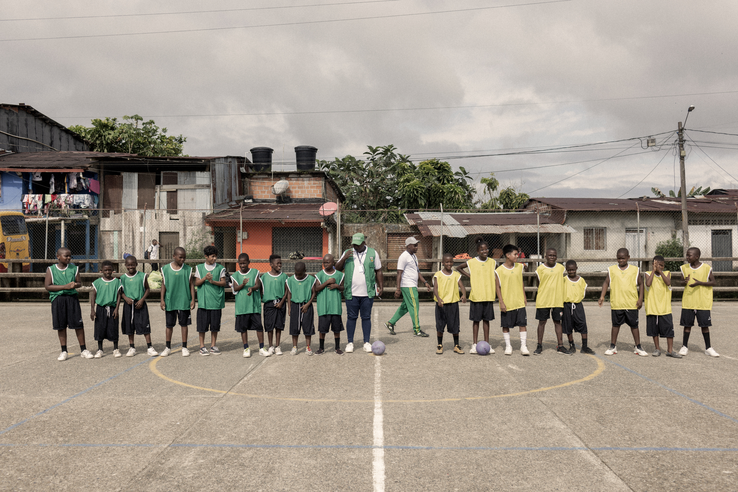 Children wearing green bibs on one side and yellow bibs on the other prepare to play a game of football.